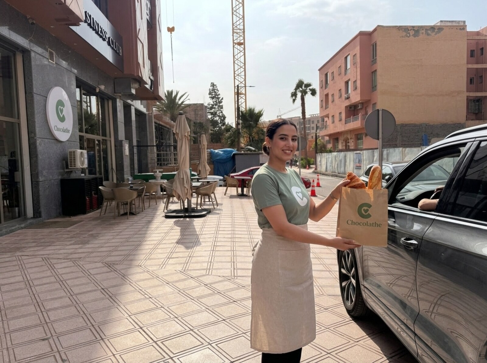 Drive boulangerie Chocolathé Guéliz Marrakech : employée apportant un sachet kraft de viennoiseries et baguette directement à la voiture d'un client garé devant le 16 Rue Ibn el Benna
